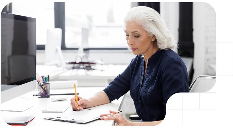 Mujer mayor escribiendo en un portapapeles en su escritorio de oficina.