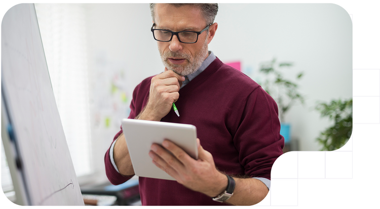 Profesional analizando datos en una tablet frente a una pizarra.